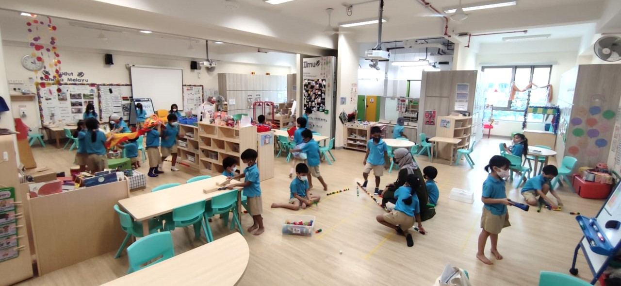 Classroom with many children in blue uniforms playing with toys at tables and on the floor.